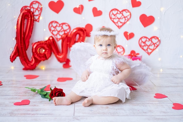 Una bambina carina in un costume da angelo con le ali su uno sfondo di cuori rossi e la scritta ama il concetto di san valentino il giorno di san valentino