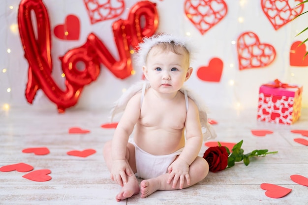 una bambina carina in un costume da angelo con le ali su uno sfondo di cuori rossi e la scritta amore. il concetto di san valentino, san valentino