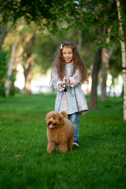 Una bambina carina in una passeggiata con il cane barboncino giocattolo È primavera fuori