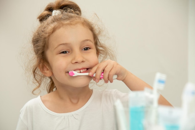 Una bambina carina si guarda allo specchio e si lava i denti in bagno