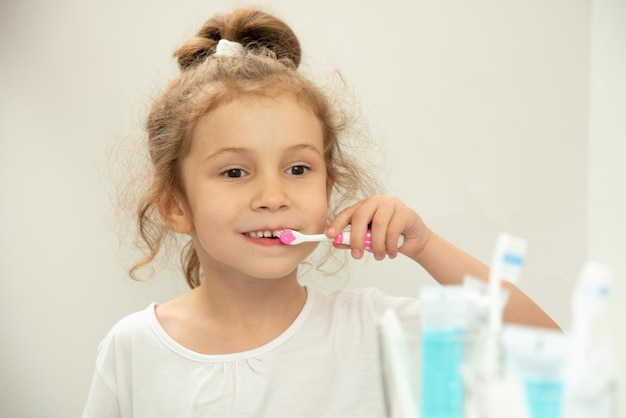 Una bambina carina si guarda allo specchio e si lava i denti in bagno