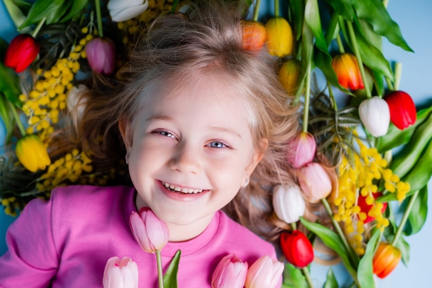 Una bambina carina si trova tra i tulipani su sfondo blu in studio.