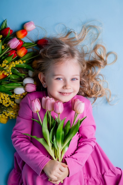 Una bambina carina si trova tra i tulipani su sfondo blu in studio.