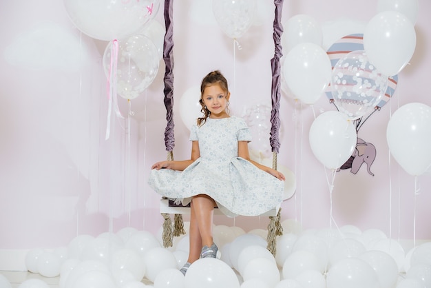 Una bambina carina sorride e posa contro il muro di un'altalena con palloncini.