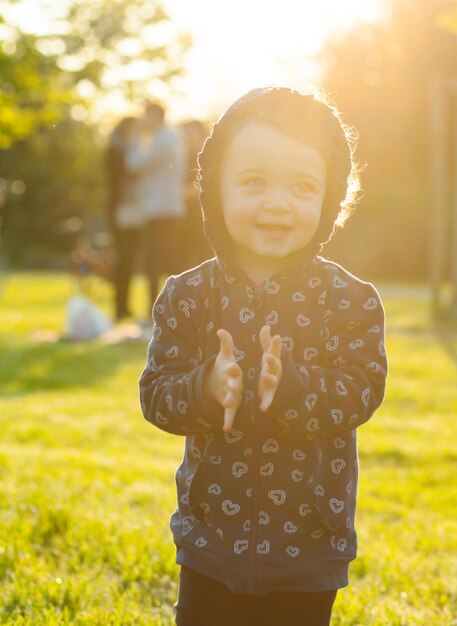 Una bambina carina sorridente in piedi nel parco al tramonto