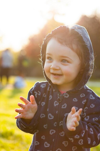 Una bambina carina sorridente in piedi nel parco al tramonto