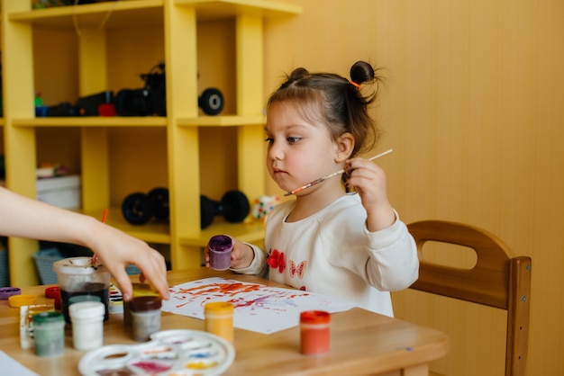 Una bambina carina sta giocando e dipingendo nella sua stanza. Ricreazione e intrattenimento.