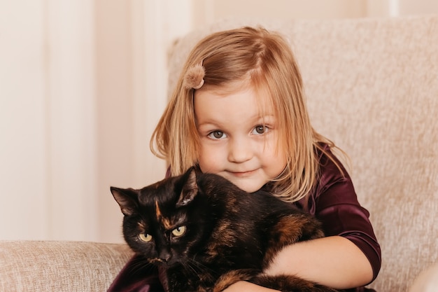 Una bambina carina tiene in braccio un gatto nero. Ragazza a casa con il suo animale domestico. La bambina ama il suo gattino carino.