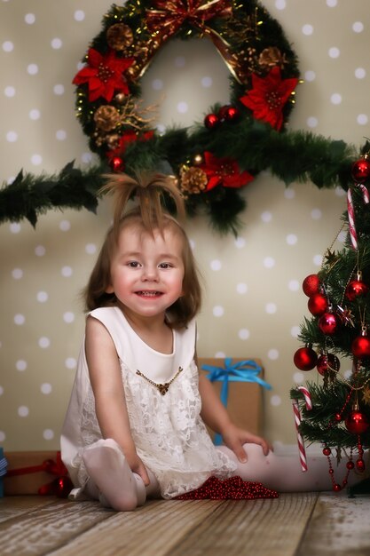 Una bambina carina veste l'albero di Natale sul pavimento della stanza