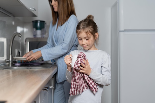 Una bambina caucasica asciuga i piatti in cucina pulendo con un asciugamano da cucina Concetto di aiuto dei genitori Copia spazio