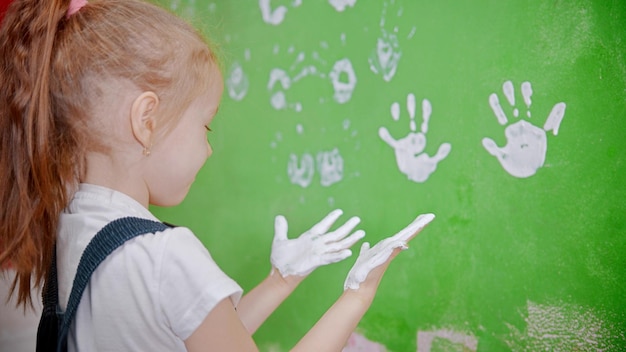 Una bambina che timbra le sue impronte di mani sul muro e si guarda le mani