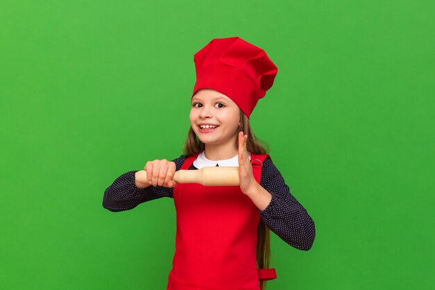 Una bambina chef in un grembiule rosso e un berretto da cucina che impara a cucinare su uno sfondo verde isolato Scegliere una professione per un bambino