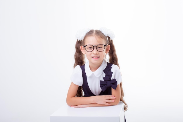 Una bambina con gli occhiali e un'uniforme scolastica è isolata su uno sfondo bianco