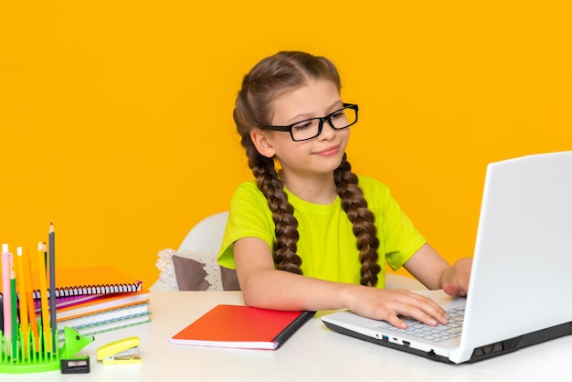Una bambina con gli occhiali sta facendo i compiti a casa alla sua scrivania Il bambino sta studiando su un laptop Istruzione online per bambini