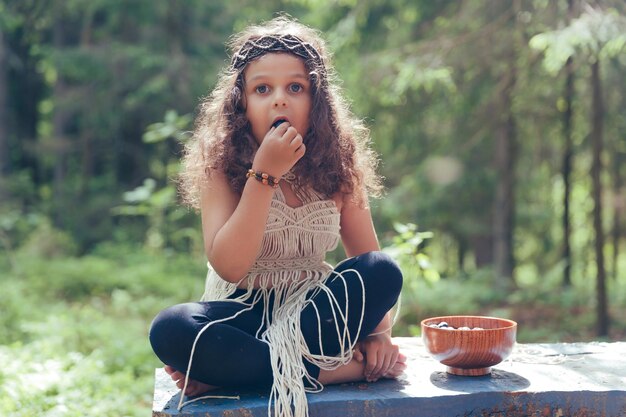 Una bambina con i capelli ricci scuri vestita da nativa della foresta mangia le bacche