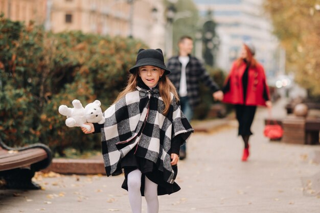 Una bambina con i suoi genitori corre nella città autunnaleUn'elegante famiglia di tre persone passeggia per la città autunnale