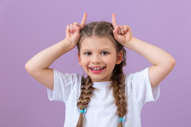 Una bambina con le trecce mostra le corna con le dita.