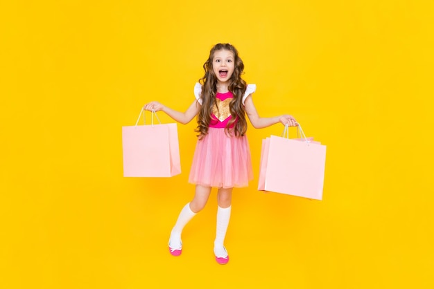 Una bambina con lo shopping a figura intera Una fashionista dopo lo shopping su uno sfondo giallo isolato Vendita per bambini La giovane principessa è felice di fare nuovi acquisti