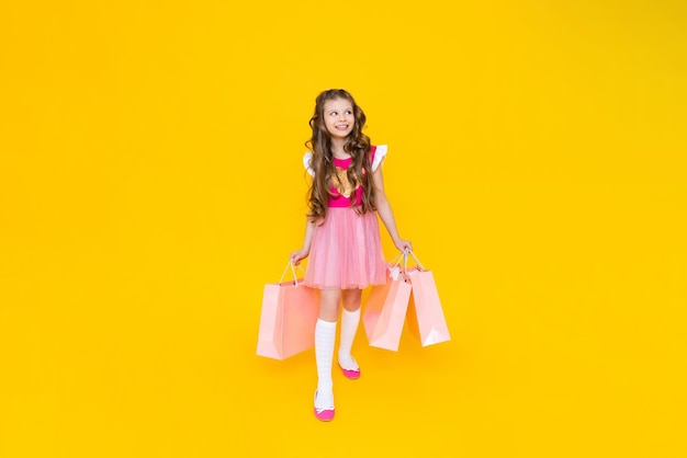 Una bambina con lo shopping a figura intera Una fashionista dopo lo shopping su uno sfondo giallo isolato Vendita per bambini La giovane principessa è felice di fare nuovi acquisti