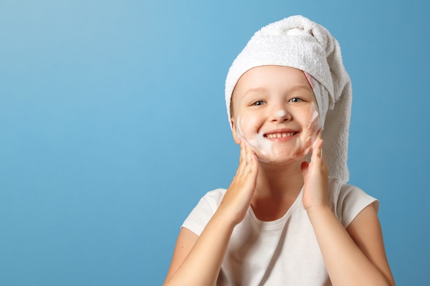 Una bambina con un asciugamano in testa si lava il viso.