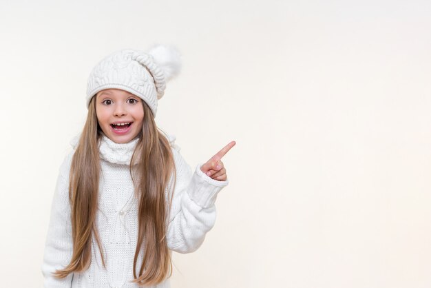 Una bambina con un caldo maglione bianco e un cappello invernale punta il dito sulla pubblicità.