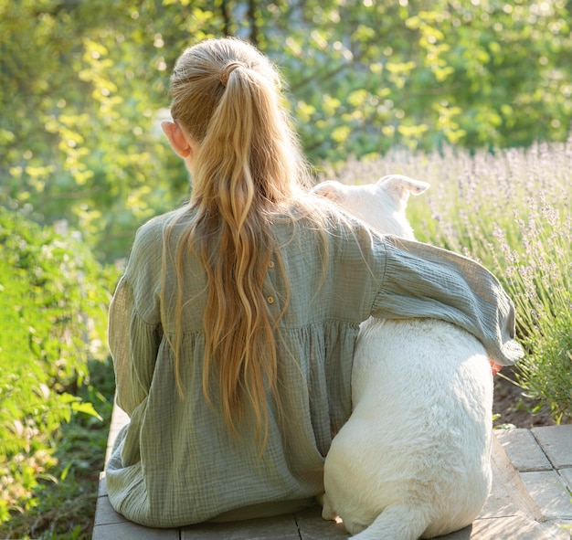 Una bambina con un cane bianco si siede e ammira il campo di lavanda