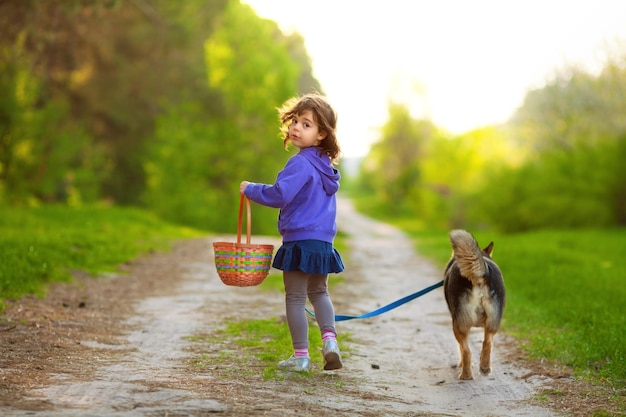 Una bambina con un cane cammina lungo la strada sterrata in campagna