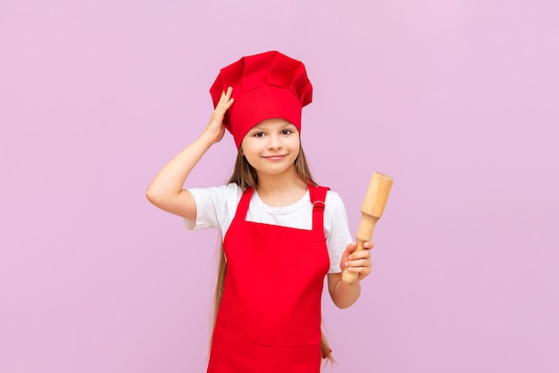 Una bambina con un cappello da chef si sta preparando per la cottura tenendo un mattarello nelle sue mani per stendere la pasta Baby Baker su uno sfondo rosa isolato