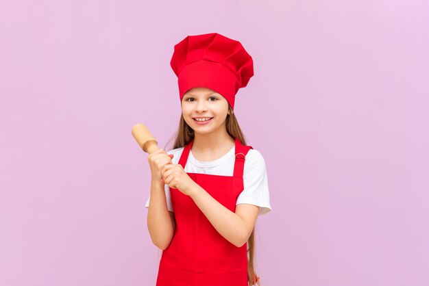 Una bambina con un cappello da chef si sta preparando per la cottura tenendo un mattarello nelle sue mani per stendere la pasta Baby Baker su uno sfondo rosa isolato