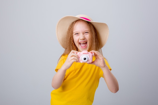 Una bambina con un cappello da viaggiatore tiene in mano una macchina fotografica su uno sfondo bianco