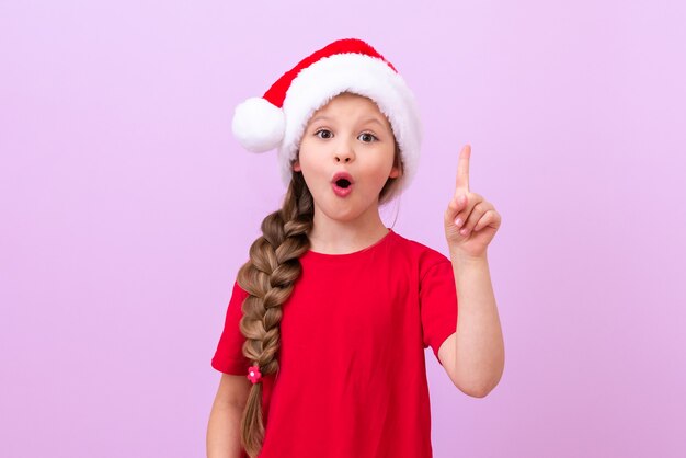 Una bambina con un cappello di Natale in testa punta il dito verso l'alto.