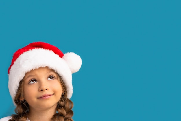 Una bambina con un cappello di Natale posa su un blu.