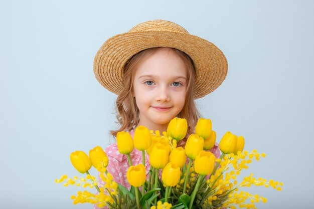 Una bambina con un cappello di paglia tiene in mano un mazzo di tulipani gialli isolati su uno sfondo bianco
