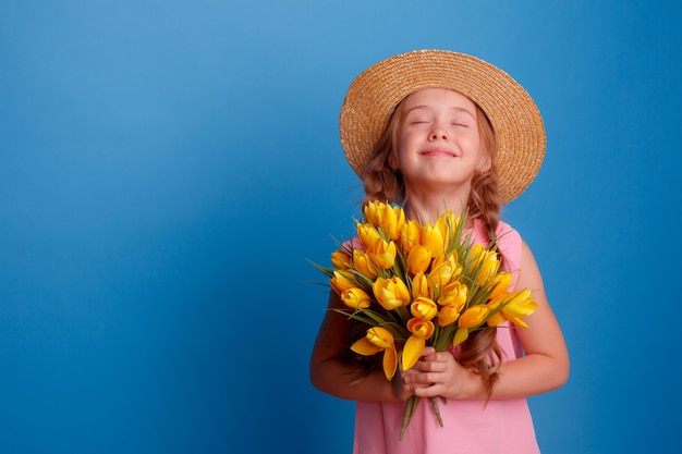 Una bambina con un cappello di paglia tiene un mazzo di tulipani gialli