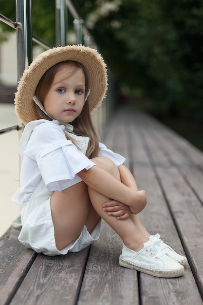 Una bambina con un cappello guarda la telecamera con la mano sul viso.