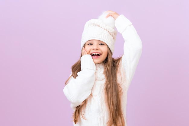 Una bambina con un cappello invernale tiene una mano sulla guancia e l'altra sul cappello