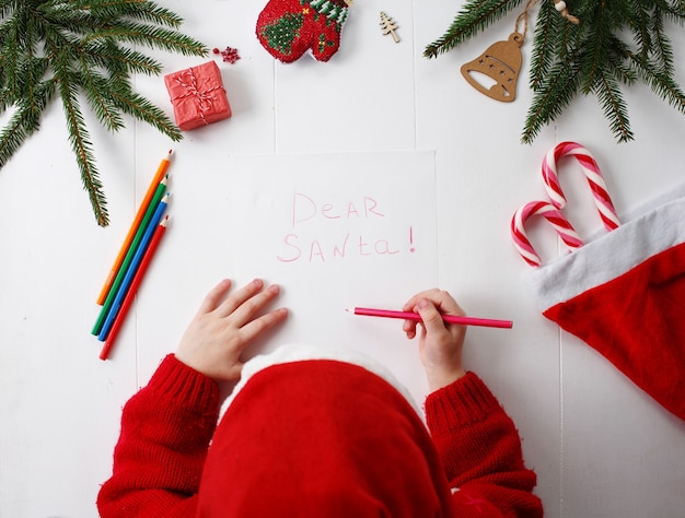 Una bambina con un cappello rosso di Natale scrive una lettera a Babbo Natale.