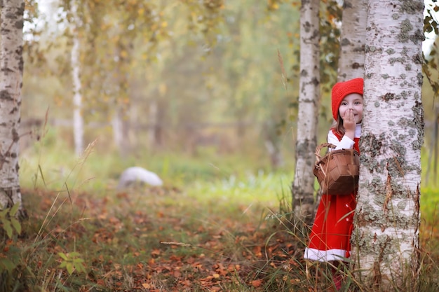 Una bambina con un cappello rosso e vestiti sta camminando nel parco. Cosplay per l'eroe delle fiabe "Cappuccetto Rosso"