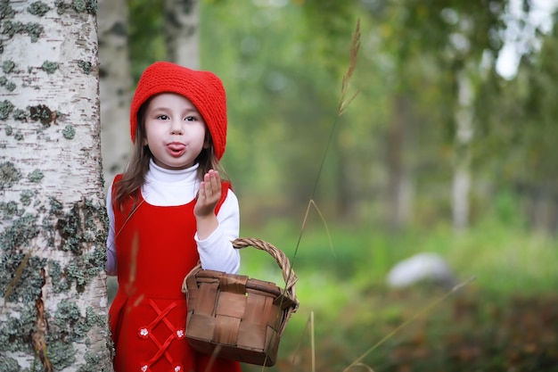 Una bambina con un cappello rosso e vestiti sta camminando nel parco. Cosplay per l'eroe delle fiabe "Cappuccetto Rosso"