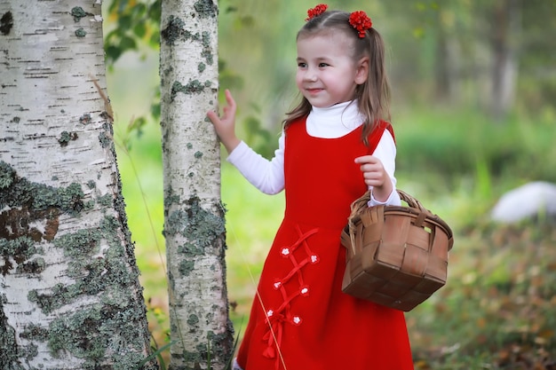 Una bambina con un cappello rosso e vestiti sta camminando nel parco Cosplay per l'eroe delle fiabe Cappuccetto Rosso