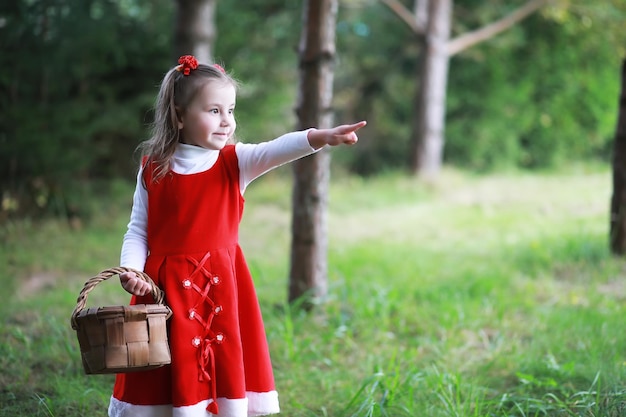 Una bambina con un cappello rosso e vestiti sta camminando nel parco Cosplay per l'eroe delle fiabe Cappuccetto Rosso