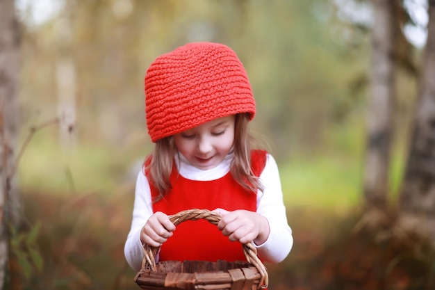 Una bambina con un cappello rosso e vestiti sta camminando nel parco Cosplay per l'eroe delle fiabe Cappuccetto Rosso