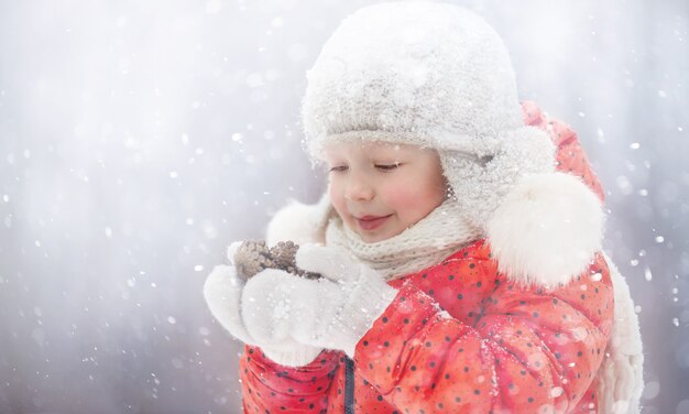 una bambina con un cappello soffice cammina in una giornata invernale innevata