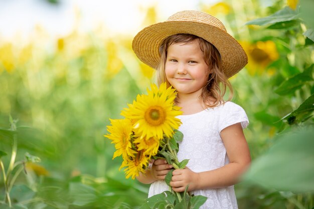 Una bambina con un cappello tiene un mazzo di girasoli in un campo di girasoli