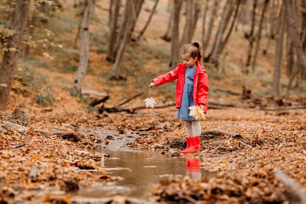 Una bambina con un cappotto e stivali di gomma rossi che camminano nella foresta autunnale. Foto di alta qualità