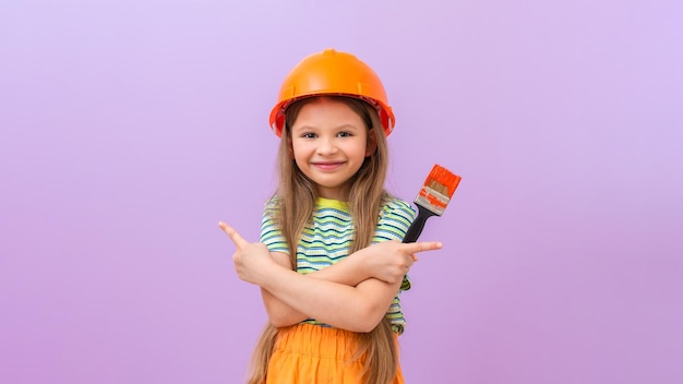 Una bambina con un casco da cantiere e un pennello in mano. lei punta le dita in direzioni diverse.