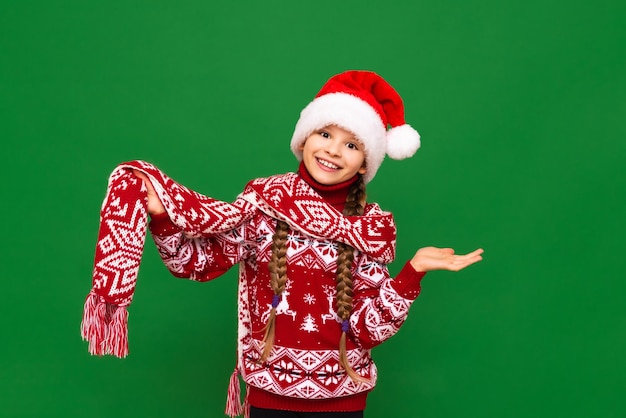 Una bambina con un maglione natalizio festivo e una sciarpa su uno sfondo verde isolato è molto felice della vacanza