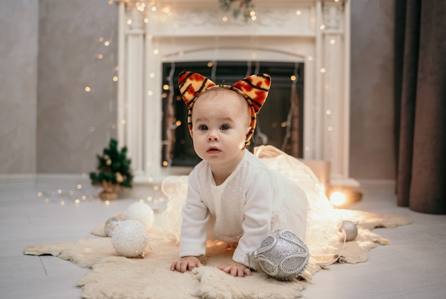 Una bambina con un soffice abito bianco e orecchie di tigre striscia sul tappeto della stanza