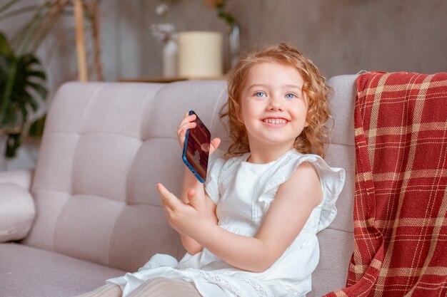 Una bambina con un telefono è seduta sul divano