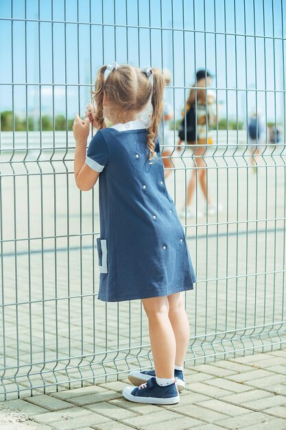 una bambina con un vestito blu si trova vicino alla barriera di un recinto a maglie alte all'aeroporto